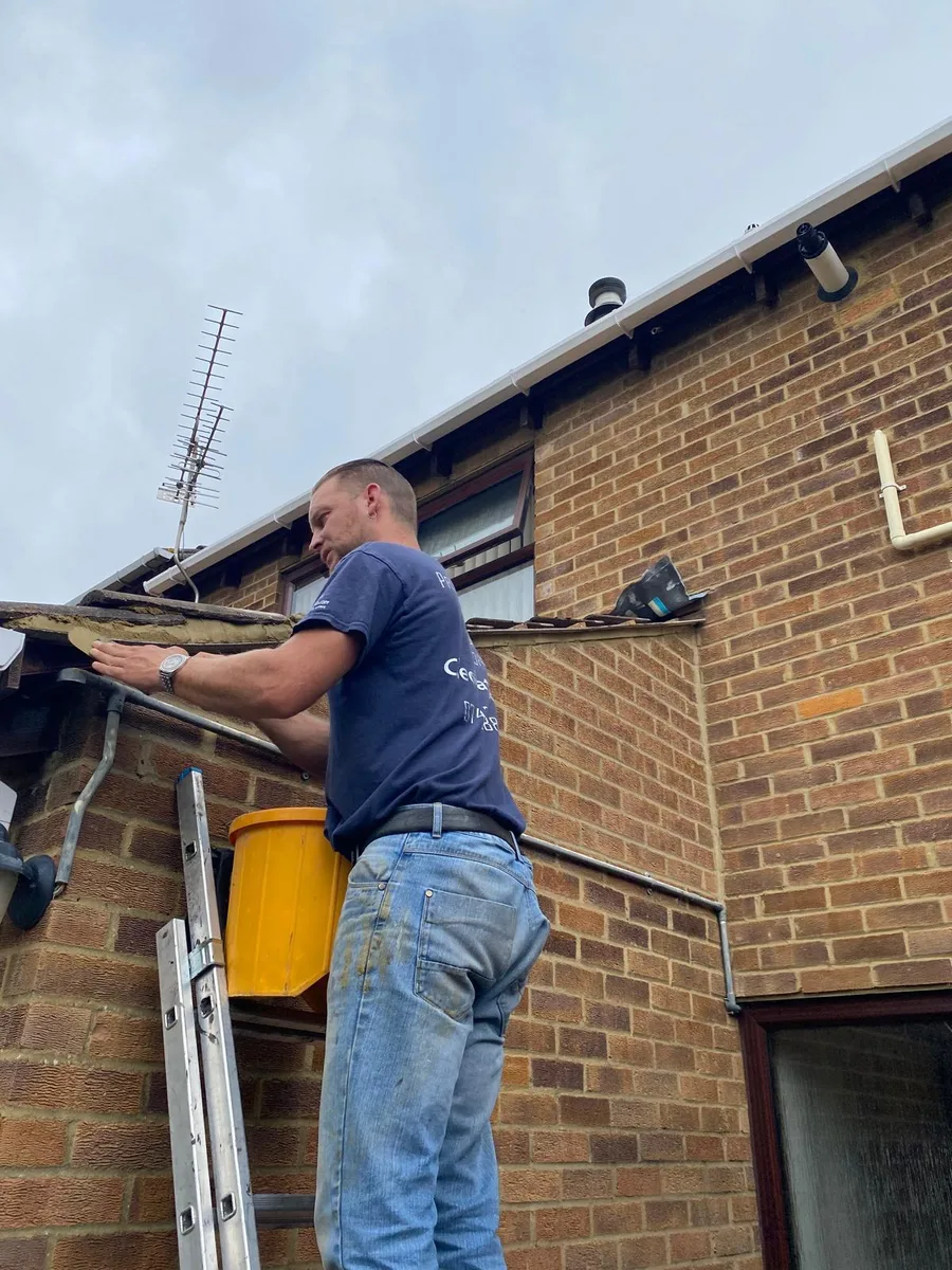 A roofer fitting new guttering from a ladder